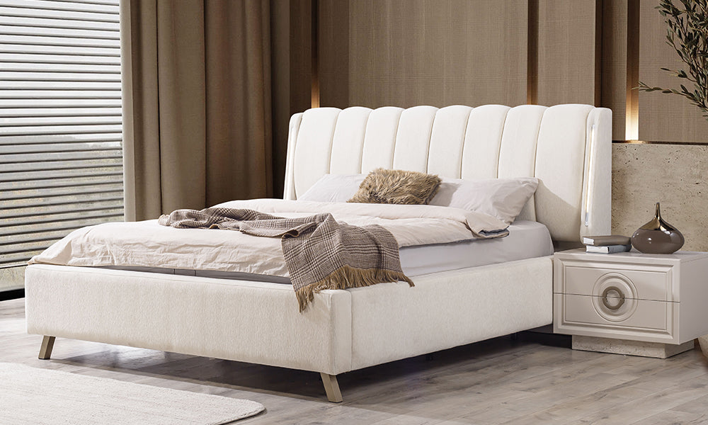 Alkan Modern Karyola; yan kanatlarında dikey LED aydınlatma bulunan krem rengi kumaş başlık, gold metal ayaklar ve lüks yatak tasarımı.