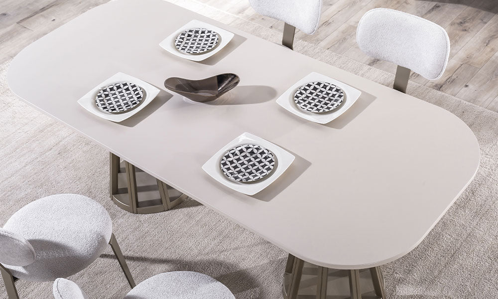 Alkan masanın geniş oval yüzeyi, leke tutmayan mat krem kaplaması ve merkezi bronz aksesuar detaylı sunum alanı.