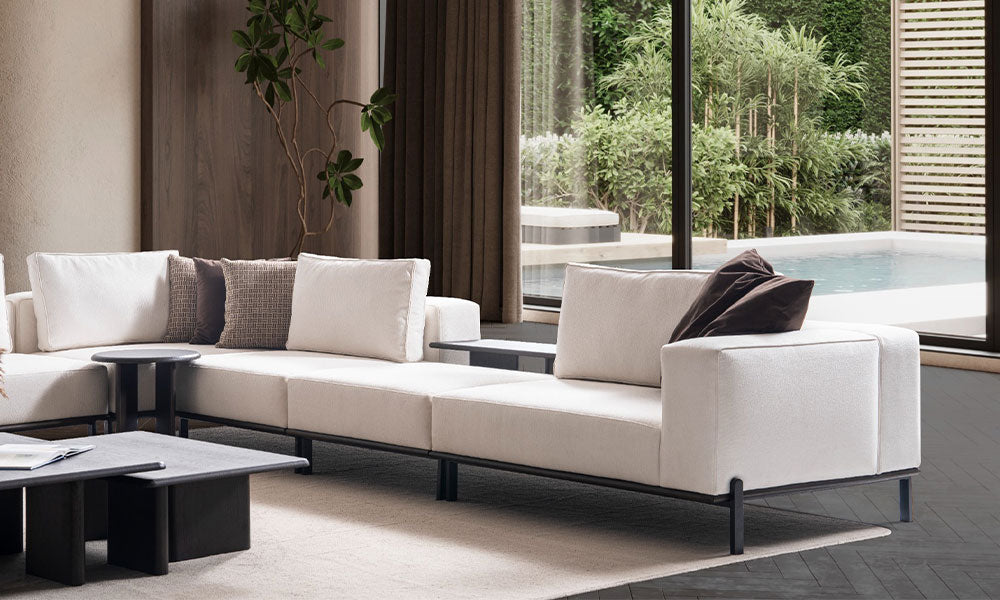 Arinna Köşe Koltuk Takımı'nın sabit sırt yapısı, ince metal ayakları ve entegre yan sehpa detayının lüks yaşam alanındaki görünümü.
