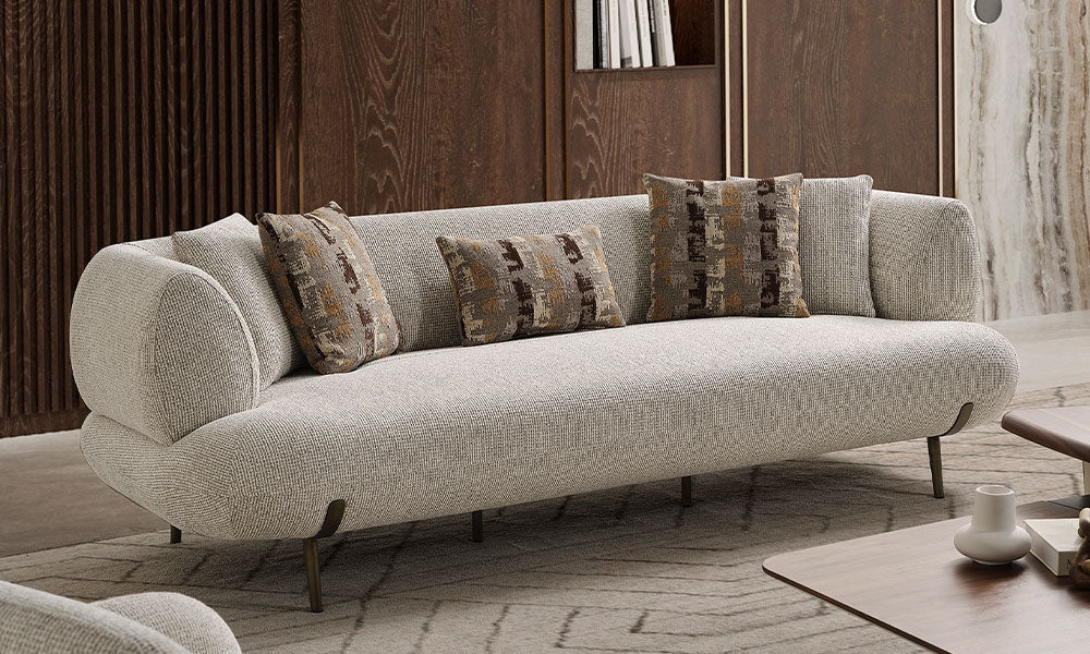 Modern bir salonda, Candy üçlü koltuğun kavisli kolçak yapısını, desenli kırlentlerini ve metal ayak detayını gösteren açı.
