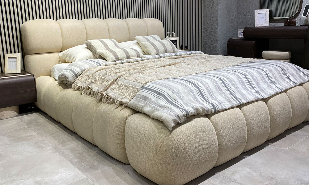Curve Modern Bazalı Karyola’nın krem döşemeli başlığı, dolgun çerçevesi ve ceviz şifonyerle birlikte görünümü
