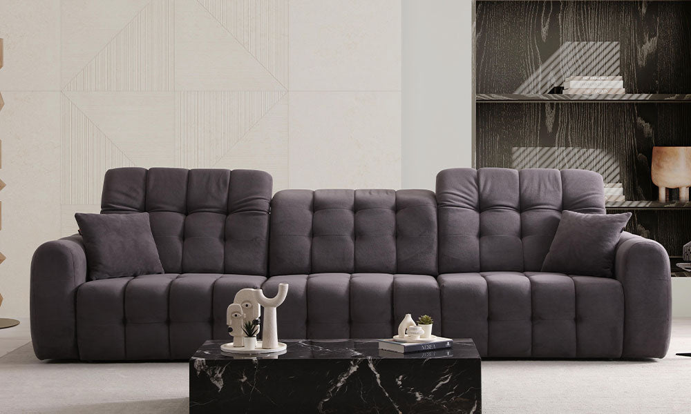 Enzo Modern dörtlü koltuğun kapitoneli ve puf tasarımlı, antrasit renkli, modern bir salondaki önden görünümü.