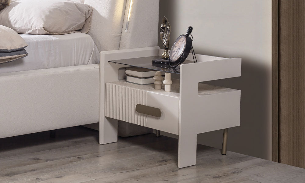 Eudora Modern Komodin; füme cam üst tablalı açık niş tasarımı, dikey fitilli krem çekmece yüzeyi, asimetrik ayak yapısı ve bronz kulp detayı.