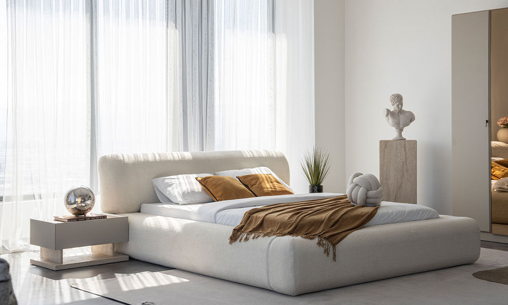 Mocha Modern Karyola'nın krem bukle kumaş kaplı, yumuşak hatlı başlığı ve odayı ferah gösteren yere yakın (low-profile) tasarımının güneş ışığındaki görünümü.