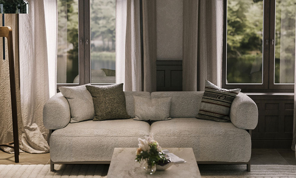 Mocha Modern üçlü koltuğun dokulu kumaşı, yuvarlak hatlı kolçakları ve konforlu yapısıyla modern bir salondaki önden görünümü.