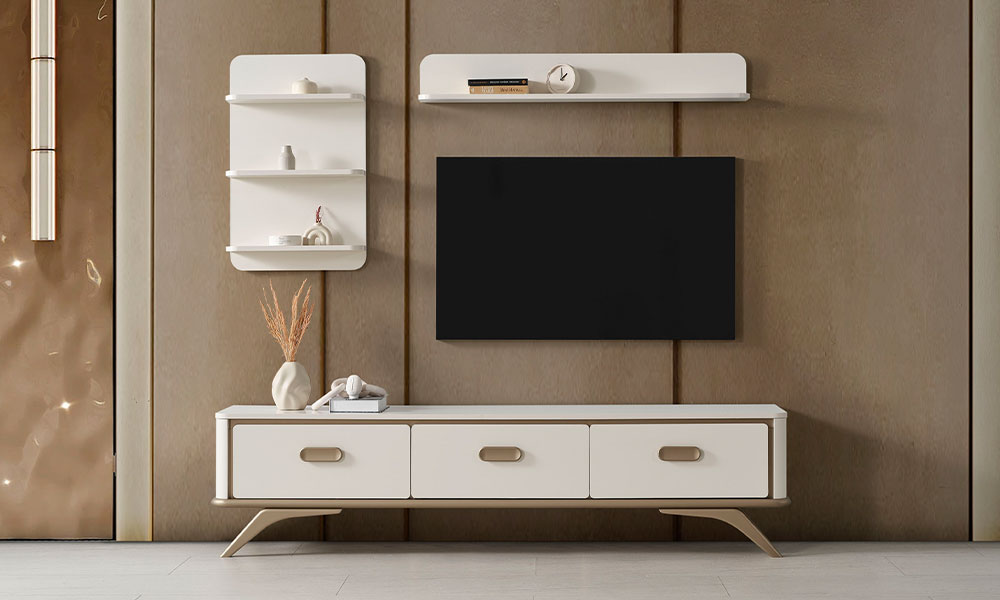 Noya Modern TV Ünitesi, krem renkli üç çekmeceli alt modülü, bronz ayakları, duvar rafları ve televizyonuyla modern salonda.