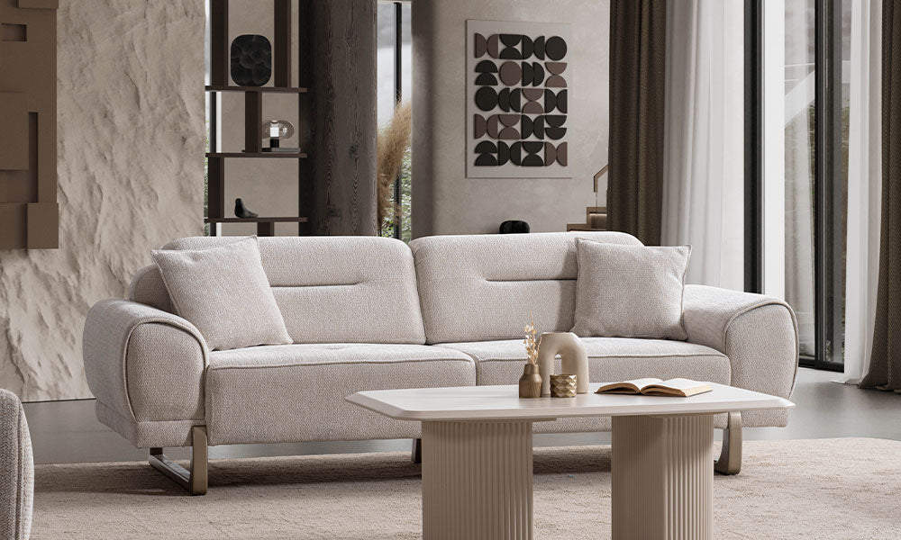 Rüya Modern üçlü koltuğun bej renkli dokuma kumaşı, kavisli kolçakları ve heykelsi ayak detaylarıyla modern bir salondaki şık görünümü.