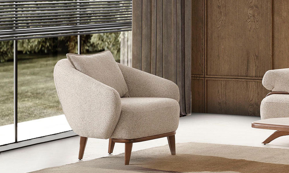 Carle Modern berjerin bej rengi dokulu kumaşı, ahşap bazası ve konik ayakları ile modern bir salondaki şık görünümü.