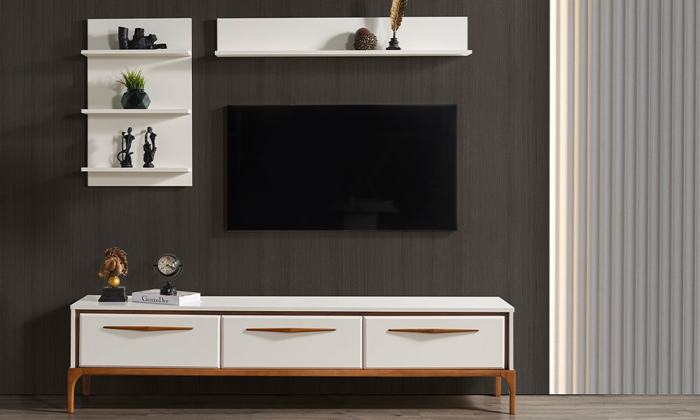 Masal modern TV ünitesi; krem renkli üç çekmeceli alt modül, ahşap ayak ve kulp detayları ile duvara monte dekoratif raflardan oluşan önden görünüm