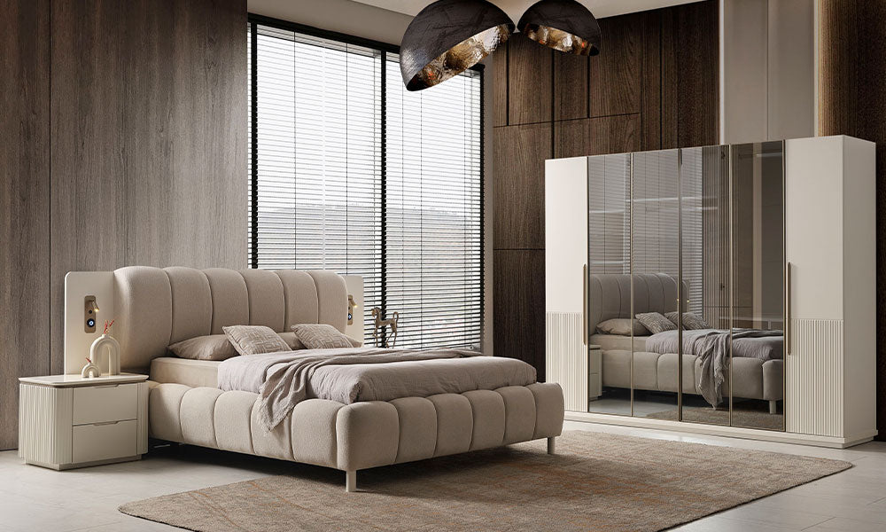Modern bir yatak odasında, New Golden koleksiyonuna ait krem renkli puf karyola, dikey yivli gardırop ve komodinlerin şık ve aydınlık duruşu.