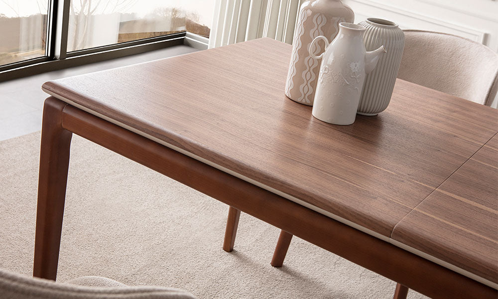 New Rivas masanın çizilmeye dayanıklı ceviz görünümlü üst yüzeyi, bej renkli alt çerçeve detayı ve pürüzsüz kenar işçiliğinin yakın plan çekimi.