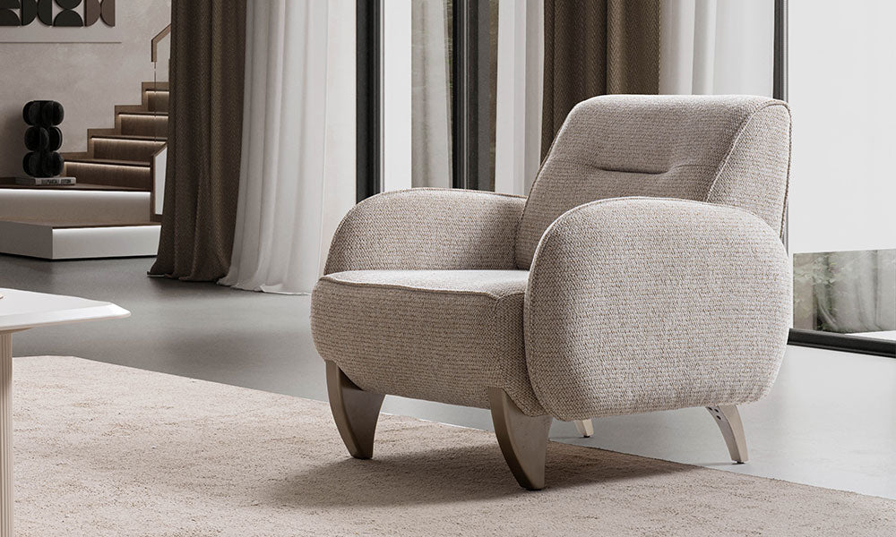 Rüya Modern berjerin bej renkli dokuma kumaşı, yatay dikişli sırt detayı ve heykelsi kalın kavisli ayaklarıyla modern bir salondaki şık görünümü.