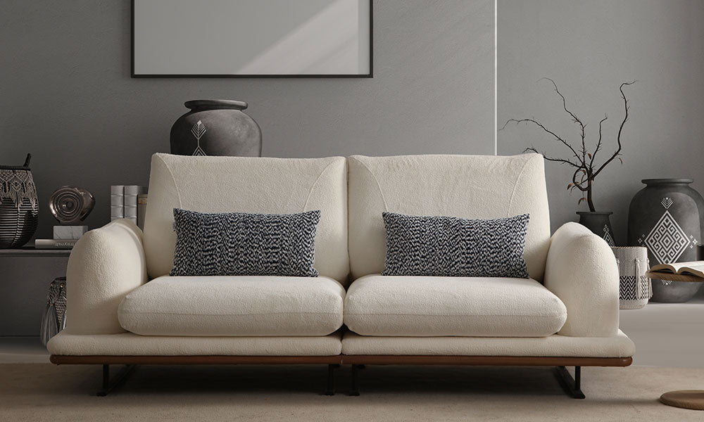 Soho Modern üçlü koltuğun krem rengi bukle kumaşı, kazayağı desenli kırlentleri ve metal ayaklarıyla modern bir salondaki önden görünümü.