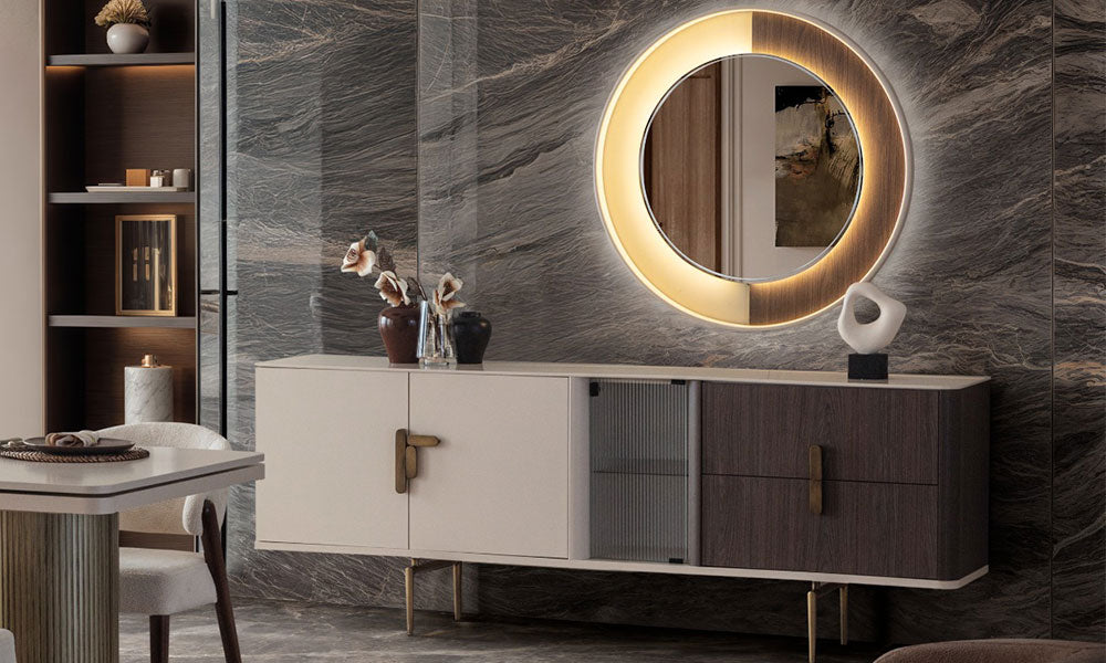 Velar Modern konsolun lüks bir yemek odasındaki görünümü; LED aydınlatmalı yuvarlak ayna, bej ve koyu ahşap renkli gövde ve füme cam kapak.