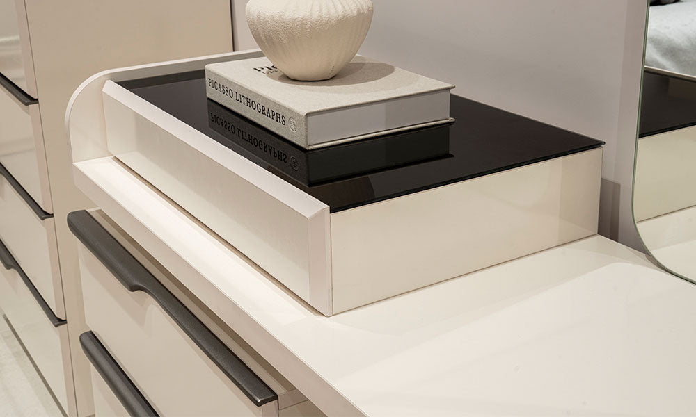 Vena şifonyerin çizilmeye dayanıklı krem yüzeyi, modern füme renkli kulpları ve takı çekmecesi üstündeki camlı/parlak detay.